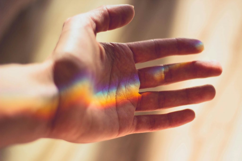 A hand with a beautiful rainbow light refraction across the palm.